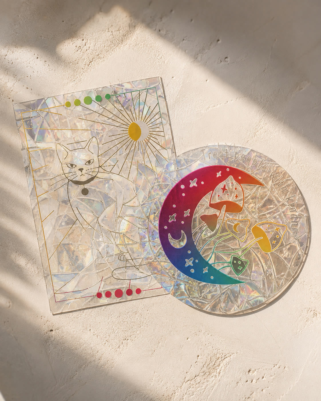Two Glimmerprism suncatcher stickers laid out in afternoon sunlight