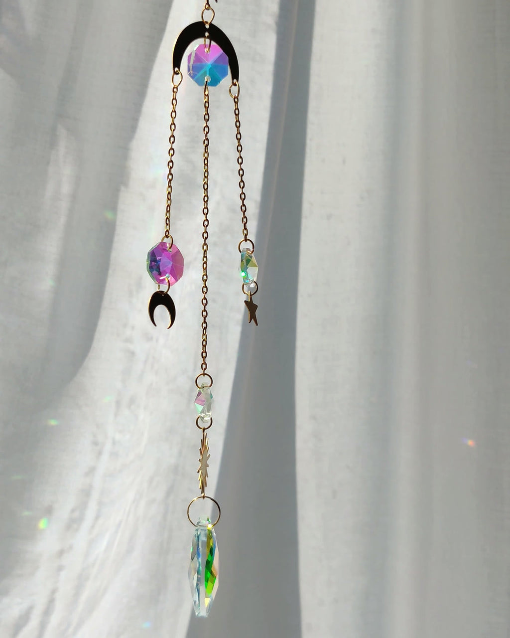 Hanging crystal with moon and star charms scattering light on a curtain