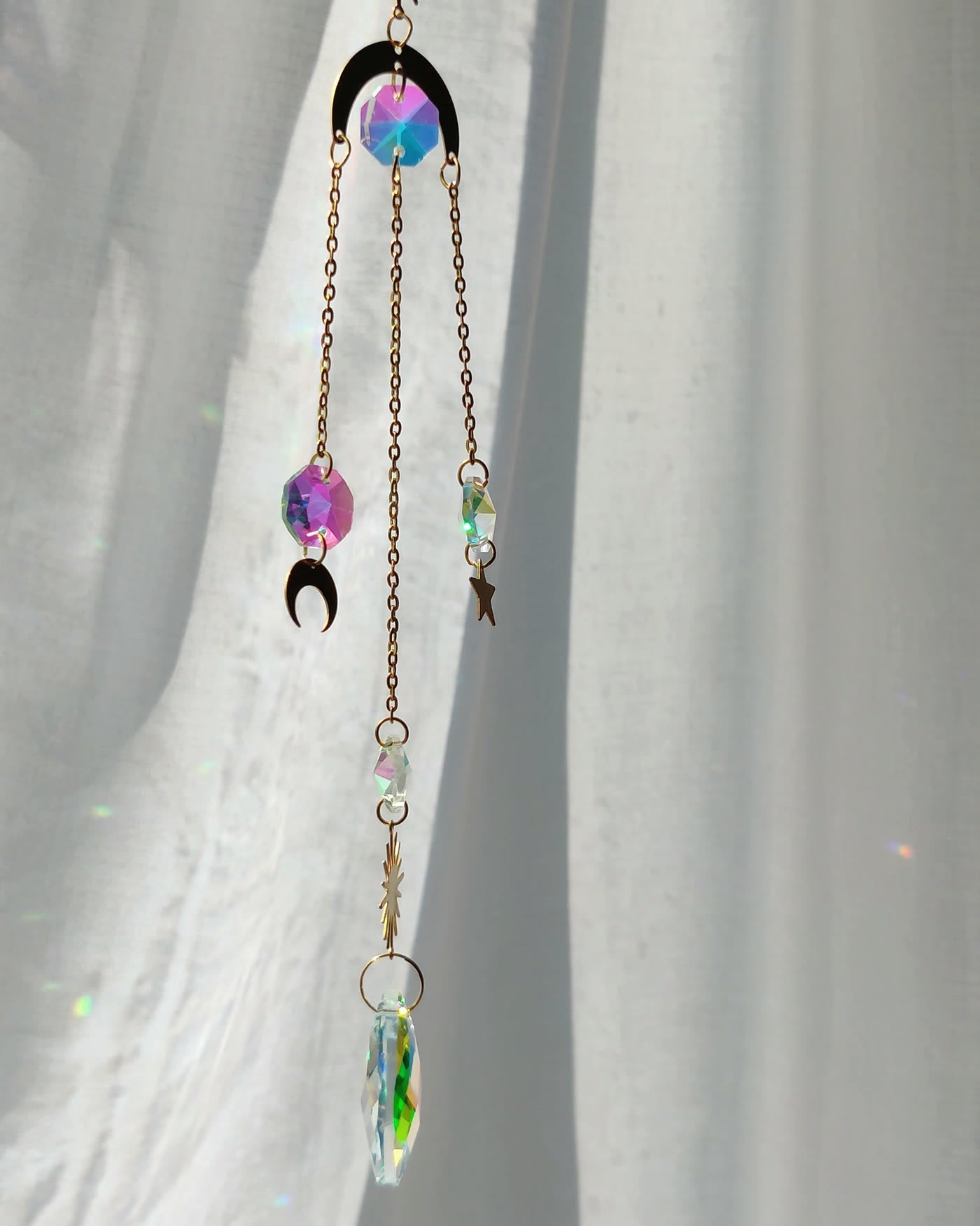 Hanging crystal with moon and star charms scattering light on a curtain