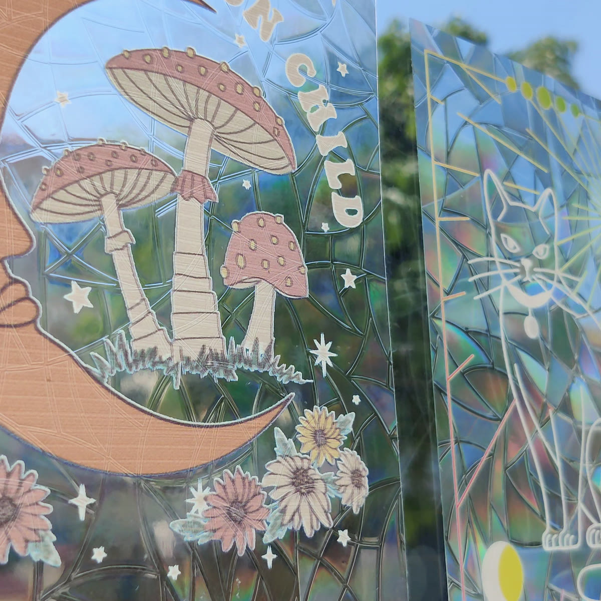 Two suncatcher designs side by side on a window in direct sun